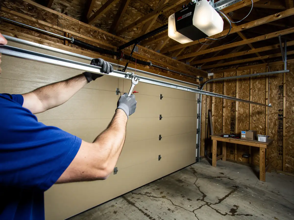 A technician in a blue shirt is adjusting a garage door track with a wrench.